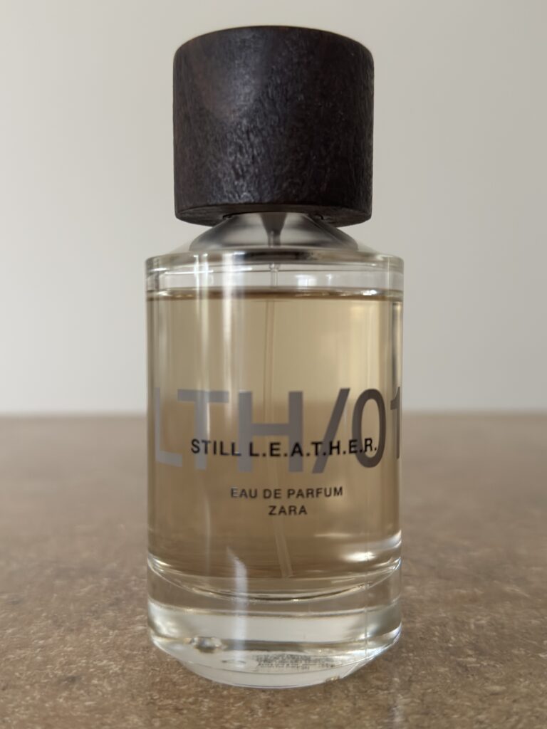 Zara Still Leather perfume bottle photographed indoors under soft lighting, showing the clean glass design and wooden cap in detail.