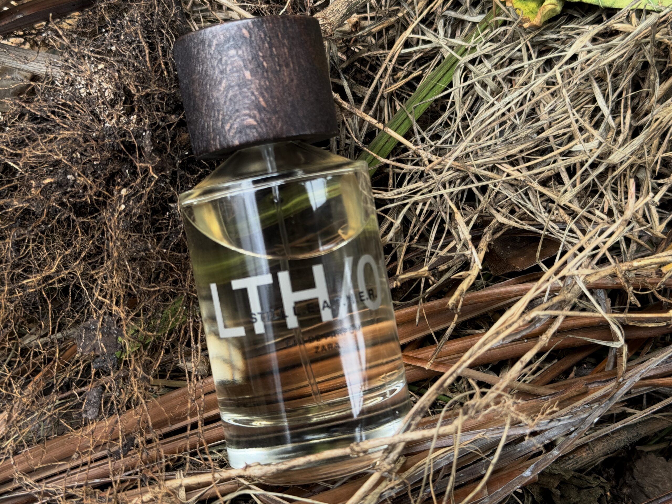 Zara Still Leather perfume bottle placed on hay outdoors, highlighting the rugged leather-inspired character of the fragrance in natural light.